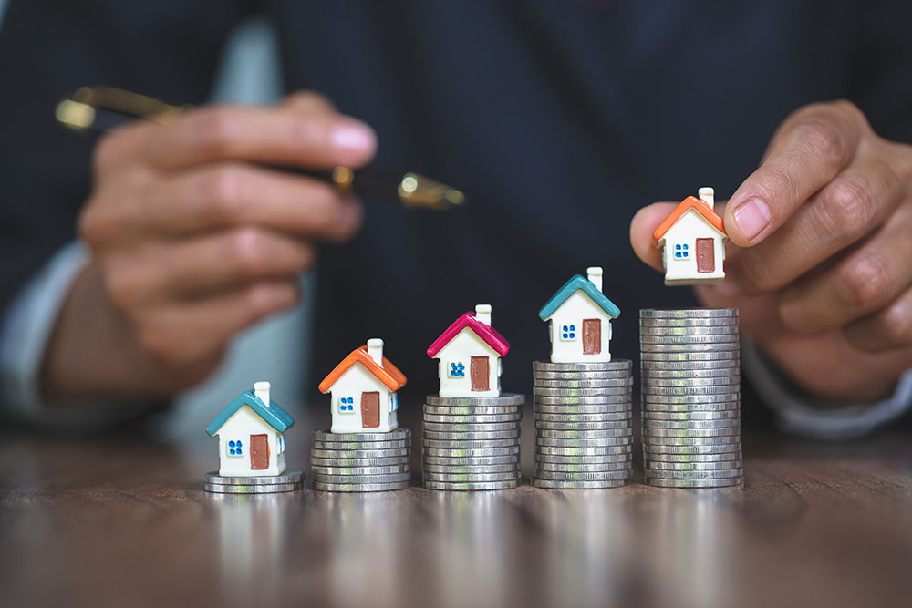 Woman hand hold a home model put on the stack coin with growing value - increase property value through building inspections