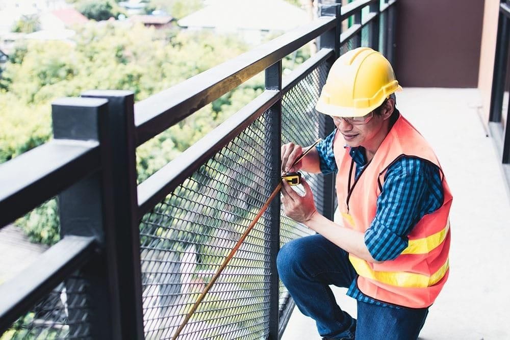 Inspector measuring balcony railing on an exterior elevated element during a structural safety inspection